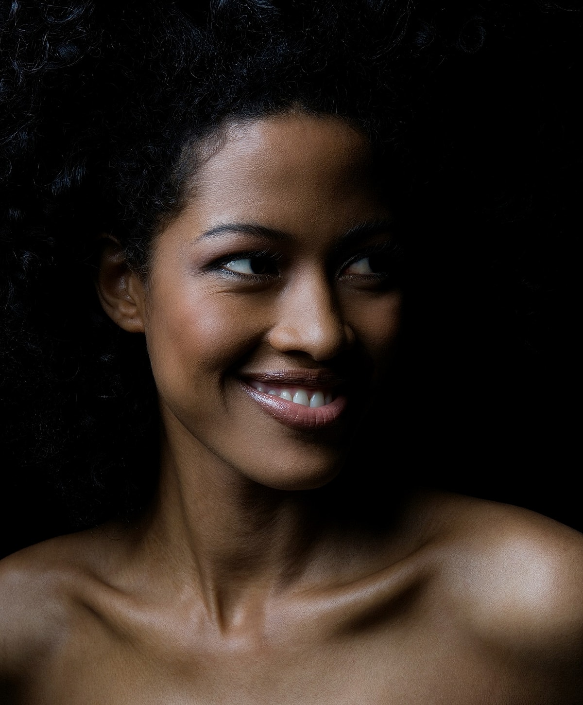 Smiling woman with curly hair against dark background.