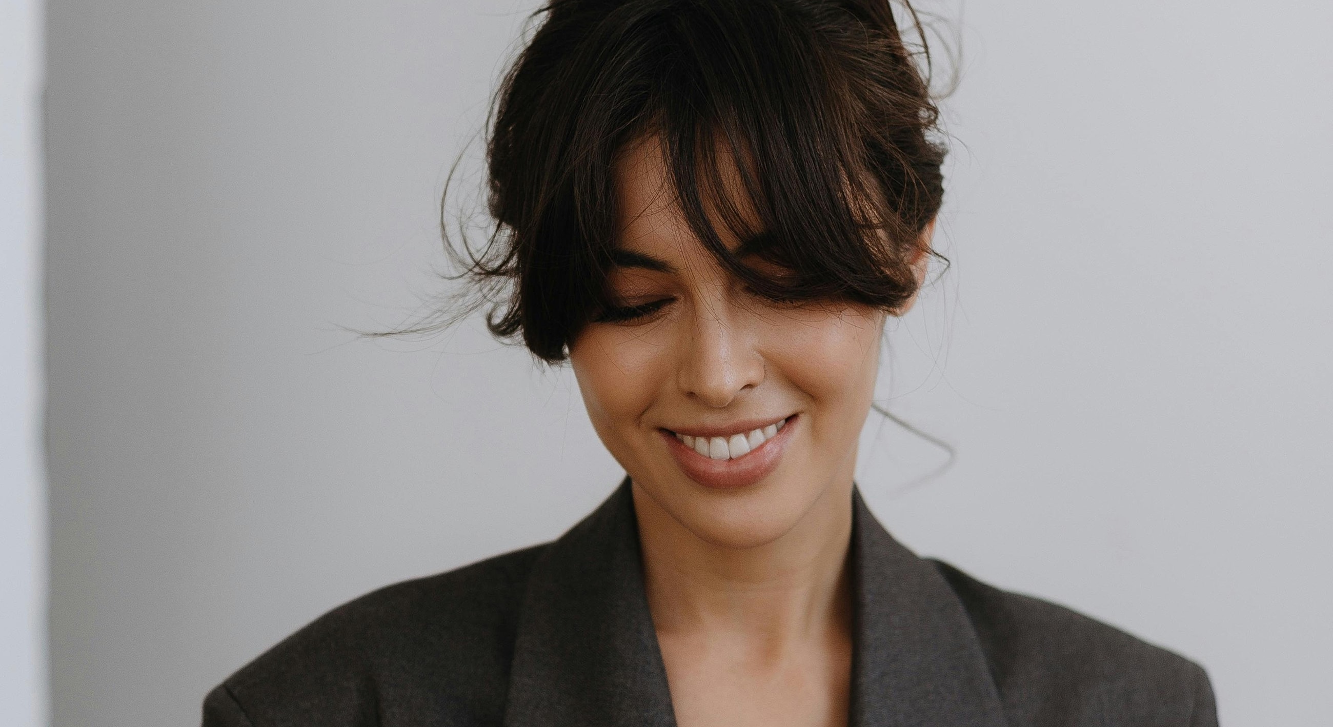 Smiling woman in blazer against neutral background.