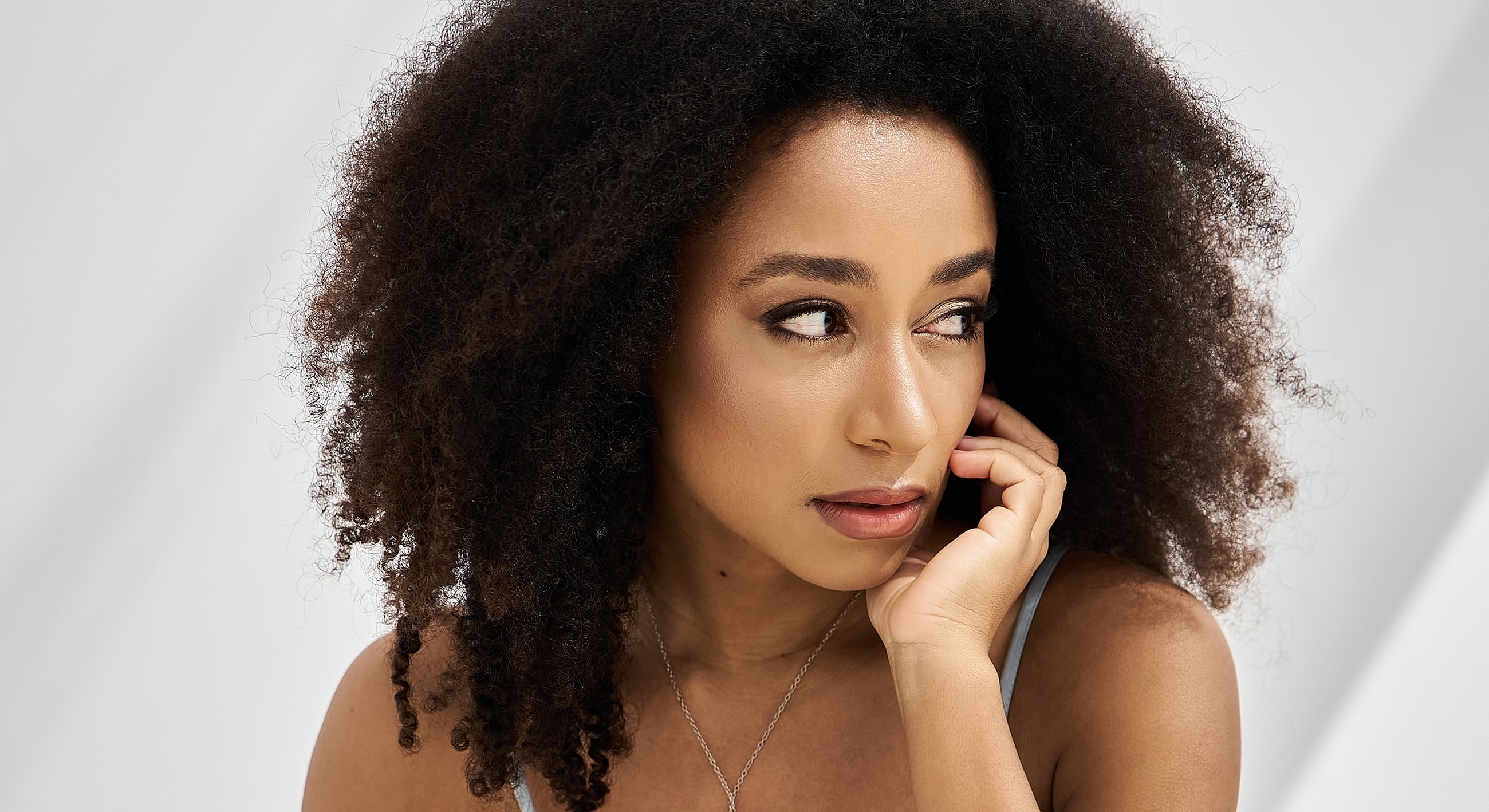 Smiling woman with curly hair and thoughtful expression.